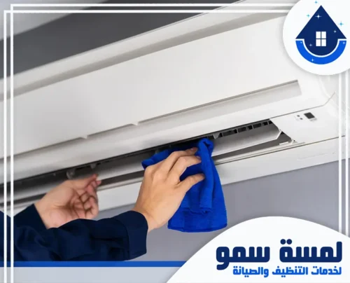 غسيل مكيفات بجدة 0554516792 لمسة سمو عامل يقوم بتنظيف وحدة تكييف داخلية بقطعة قماش زرقاء، ضمن خدمات شركة لمسة سمو