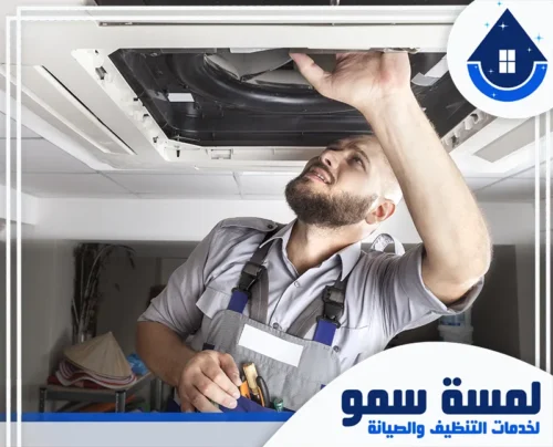 صيانة مكيفات جدة 24 ساعة 0554516792 لمسة سمو فني يرتدي زي العمل يقوم بفحص وإصلاح وحدة تكييف مركزية داخلية، معتمداً على خبرته الواسعة ضمن فريق لمسة سمو