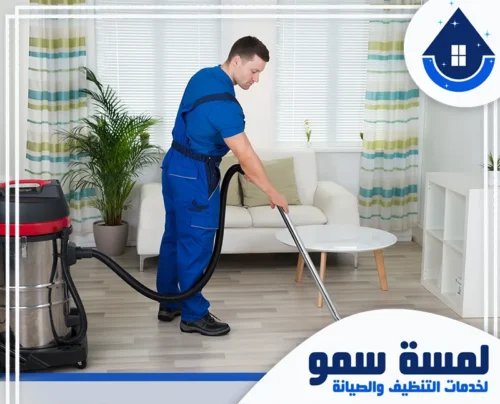 تنظيف منازل بجدة 0554516792 لمسة سمو فني تنظيف محترف يرتدي زي العمل الأزرق ويستخدم مكنسة كهربائية صناعية كبيرة لتنظيف أرضية غرفة المعيشة